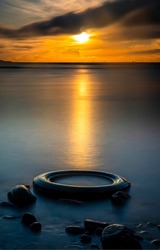 A tire in the water at sunset. Old tire in sunset water. Sunset sea scene. Tire in water at sunset