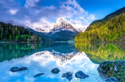 A mountain peak is reflected in a mountain lake. Beautiful mountain lake landscape. Mountain forest reflected in lake water. Forest lake in mountains
