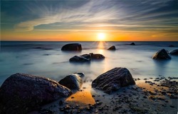Coastal boulders on the beach at dawn. Sunrise on sea beach. Early morning beach at dawn. Sea beach at dawn