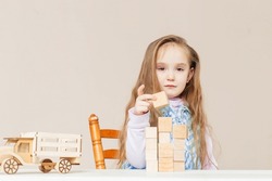 Happy cute little girl building tower from wood bricks and blocks, plays with wooden car. Kid playing active games at home, Play time concept. ECO wooden toys