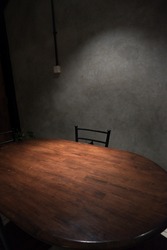 A single empty chair with a wooden table below spotlight. Illustration picture of interrogation room. Empty chair feels like horror movie background.