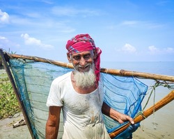 Smiling portrait of white beard muslim village fisherman fishing with a lave net in hand , rural old man is working beside a river, Bangladeshi fisherman with white dress and red towel in head