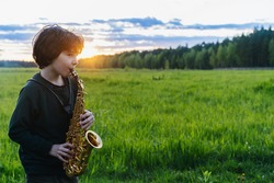 Boy plays saxophone in the sunset. Silhouette of a curly haired guy with a soprano saxophone 