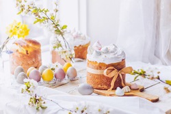 Traditional ukrainian easter cake with white swiss meringue. New cruffin cake trend 2021. Spring cherry blossom and colorful painted eggs. Person decorates cake with hand. Free copy space.