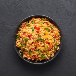 Veg Schezwan Fried Rice in black bowl at dark slate background. Vegetarian Szechuan Rice is indo-chinese cuisine dish with bell peppers, green beans, carrot. Top view