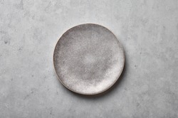 Gray ceramic plate on grey concrete rough background. Empty spotted uneven saucer. Matte dish on stone textured backdrop. Hand made ceramic table setting. Top view