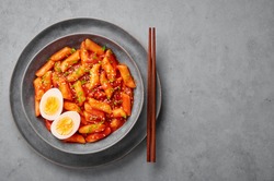 Tteokbokki with eggs in gray bowl on concrete table top. Tteok-bokki is a korean cuisine dish with rice cakes. Asian food. Top view. Copy space