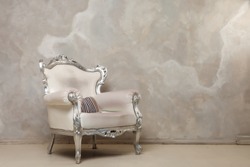 An antique white chair against the wall. Antique leather chair. There is a striped pillow on the chair