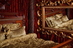 Luxury bedroom in medieval style with art Deco elements and large mirror. Bed and items with patterns. Refined interior. Comfortable king size bed in gold color. Copyright space for website or banner