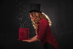 Female magician makes with soap bubbles show, an illusionist in theatrical clothes, on black background. Woman actress in stage costume. Concept of theatrical performance and fun show. Copy space