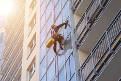Concept of industry urban works. Industrial mountaineering worker in uniform hangs over residential facade building, washing exterior glazing. Rope access laborer hangs on wall of house. Copy space