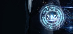 Smart businessman pointing digital dashboard in 2022 on dark blue background. Futuristic technology trend concept. Artificial intelligence (AI), machine learning support for enhancing business growth.