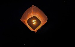 Orange sky lantern with the flames showing clearly lifting off to the dark starry sky.