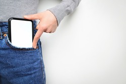 Woman puts mobile phone in jeans pocket on gray light background. Isolation, space for text. 