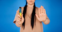 a girl on a blue background holds a disposable cigarette in one hand and shows a stop to smoking with the other hand. the concept of a healthy lifestyle.