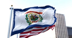 the flag of the US state of West Virginia waving in the wind with the American flag blurred in the background. West Virginia was admitted to the Union on June 20, 1863 as 35th state