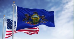 The Pennsylvania state flag waving along with the national flag of the United States of America. In the background there is a clear sky. Pennsylvania is a U.S. state in the northeast