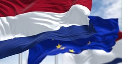 Detail of the national flag of the Netherlands waving in the wind with blurred european union flag in the background on a clear day. Democracy and politics. European country. Selective focus.