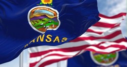 The Kansas state flag waving along with the national flag of the United States of America. In the background there is a clear sky. Kansas is a state in the Midwestern United States