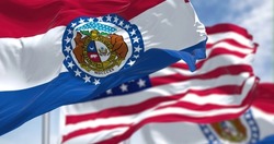 The Missouri state flag waving along with the national flag of the United States of America. In the background there is a clear sky. Missouri is a state in the Midwestern region of the United States