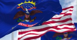 The North Dakota state flag waving along with the national flag of the United States of America. In the background there is a clear sky. North Dakota is a U.S. state in the Upper Midwest