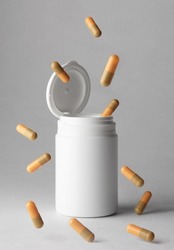 An orange-beige colored pill capsule falling out of a white plastic pill bottle on a light background.