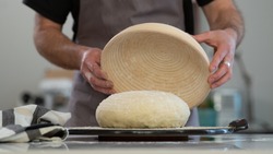 Male baker lightly flouring proofing basket for home made sourdough bread. 