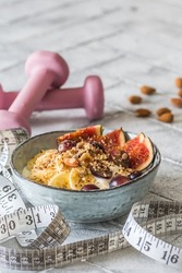 Bowl of yoghurt, fruits and nuts for a healthy diet breakfast or snack. Pink dumbbells and a tape measure on gray background, weight loss concept. Vertical with copy space.
