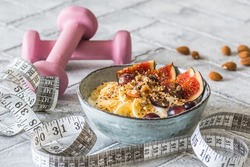 Bowl of yoghurt, fruits and nuts for a healthy diet breakfast or snack. Pink dumbbells and a tape measure on gray background, weight loss concept