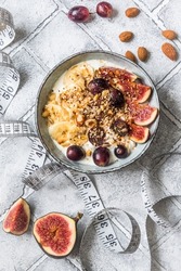 Bowl of yoghurt, fruits and nuts for a healthy diet breakfast or snack and a tape measure on gray background, weight loss concept. Top view.