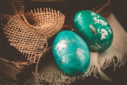 Two green and turquoise metallic Easter eggs with an antique book on a dark brown vintage background
