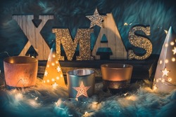 Word xmas in wooden capital letters, uppercase, and different christmas candle lights and fairy lights on a fur 