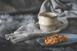 Chocolate cookies and a cup on a gray fur with woolen pullover, cozy winter coffee scene