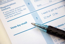 Closeup of 'Vote-by-mail' section on a voter registration form, with ballpoint pen laying on the form.