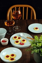 serving of strawberry jam thumbprint cookies on a plate and wooden table

served with old fashioned syrup, with family

accompanied by a unique and beautiful old school chair