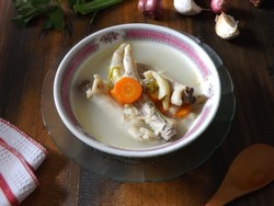 Chicken feet soup, hot and spicy  served in white bowl on wooden table. Known as sop ceker in Indonesia. Commonly mixed with vegetable such as carrot. Delicious, tasty, refreshing. Focus selection. 