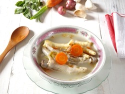 Chicken feet soup, hot and spicy  served in white bowl on wooden table. Known as sop ceker in Indonesia. Commonly mixed with vegetable such as carrot. Delicious, tasty, refreshing. Focus selection. 