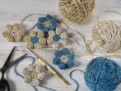  Crochet flower, crochet hook, and balls of yarn on white wooden table. Crochet project and simple handmade decoration concept. 