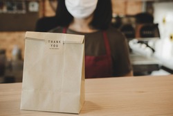 waitress wearing protection face with dessert paper set bag on counter bar waiting for customer in modern cafe coffee shop, food delivery, cafe restaurant, takeaway food, small business owner concept