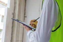 home inspector engineer in green reflective jacket checking review document and inspecting with clipboard at construction site building interior, construction, contractor and engineering concept