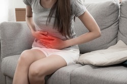 asian young woman suffering stomach ache sitting on couch in living room at home, people painful stomachache, gynecology, menstrual pain , medical and health care concept