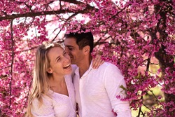 Beatiful lovely couple stay and have fun in Sakura flowers and hug each other. Wonderful flowering time of Japanese tree. Pink flowers around of woman and man.
