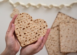 Woman's hand holds Matzah shape of heart. Traditional of Jewish Holiday on Passover. Home symbol of lovely family. top view, layout. love and care. Gift for lovers. Feeling in love and blissful life