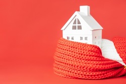 White toy house wrapped in red scarf on red background. Heating or insulating buildings or houses concept. Copy space