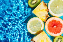 Colorful abstract image fruit citrus lemon, kiwi, orange, pineapple, grapefruit, lemon, pomelo water splashing fresh transparent surface, flecks. Flat lay, top view. Copy space. Summer beach tropical