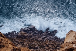 Top view of dangerous rocky beach seashore coastline surrounded by stormy waves, steep cliffs, stones boulders cobbles on windy day. Summer, holiday, travelling, seascape, landscape, nature, storm.