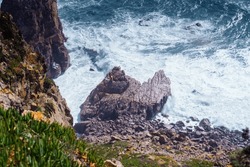 Top view of rocky beach seashore coastline surrounded by foamy waves, steep mountains cliffs covered with green grass on windy day. Summer, holiday, travelling, seascape, landscape, nature, storm.
