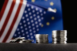 Money of the United States and Europe and two Flags on a dark background. It is a symbol of the United States of America increasing tariff tax barriers for import products from EU countries.
