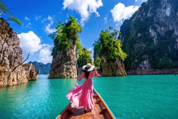 Beautiful girl standing on the boat and looking to mountains in Ratchaprapha Dam at Khao Sok National Park, Surat Thani Province, Thailand.