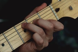 Person plucking the strings on the frets of an electric guitar. Selective focus. Copy space.